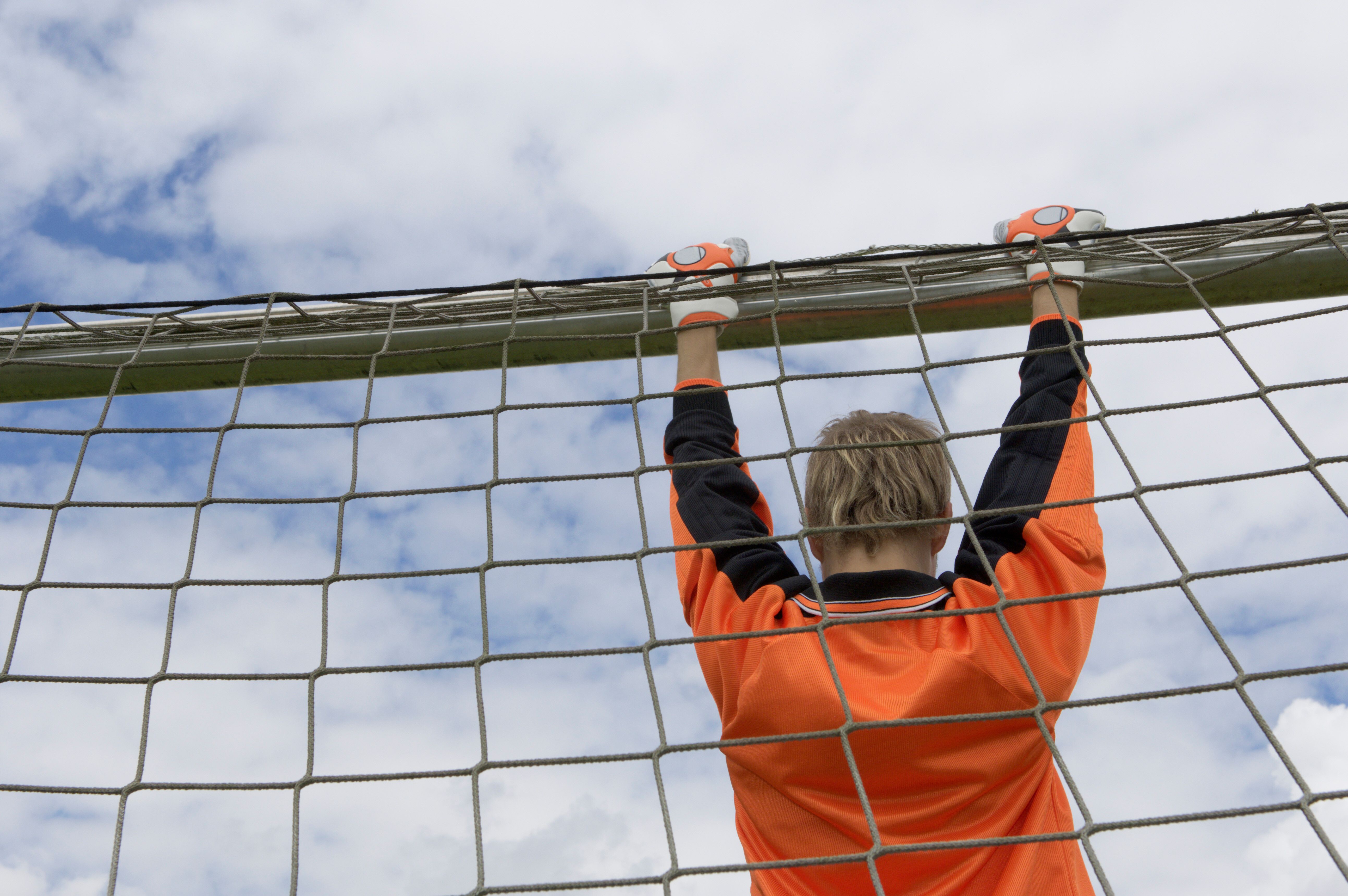 Goalkeeper in an orange shirt holding the crossbar